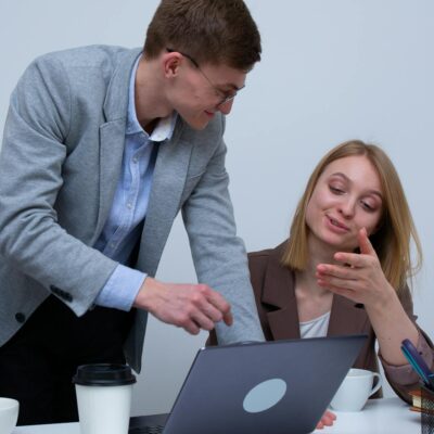 Two colleagues collaborating over laptops in a modern office setting.